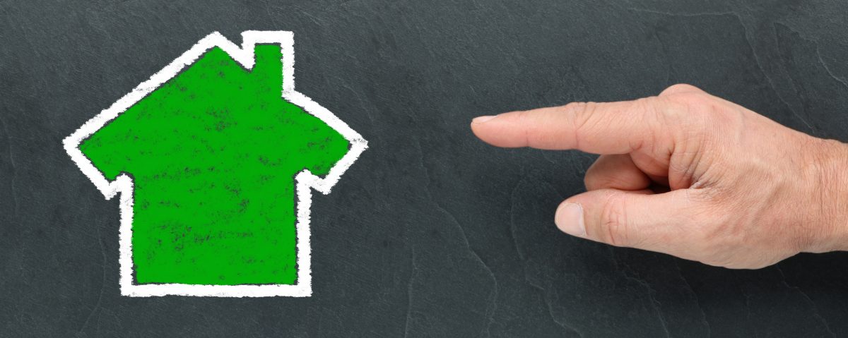 Hand die wijst naar een duidelijk getekend huis op krijtbord